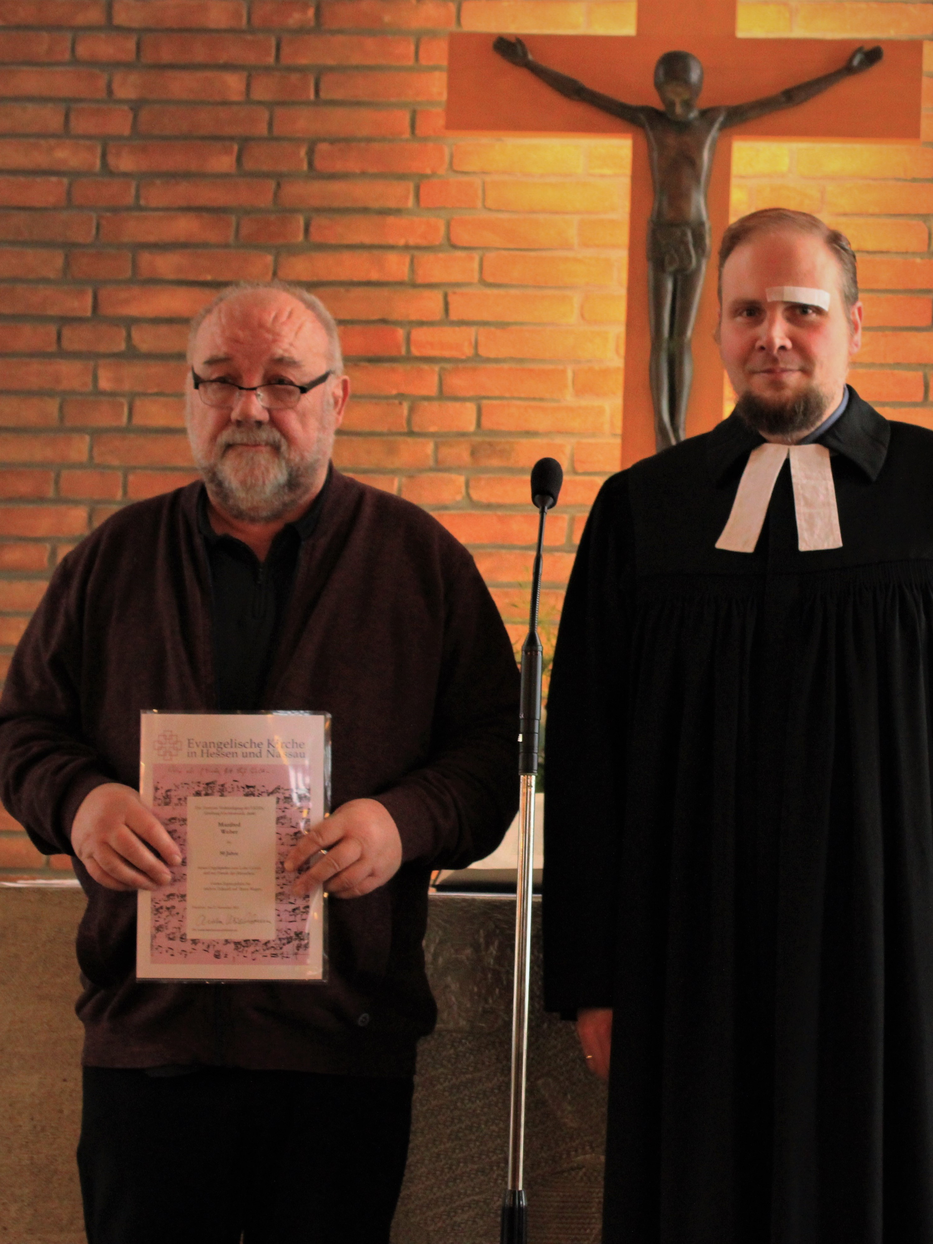 Bild von M. Weber der von Pfarrer Heinz eine Urkunde überreicht bekommt.